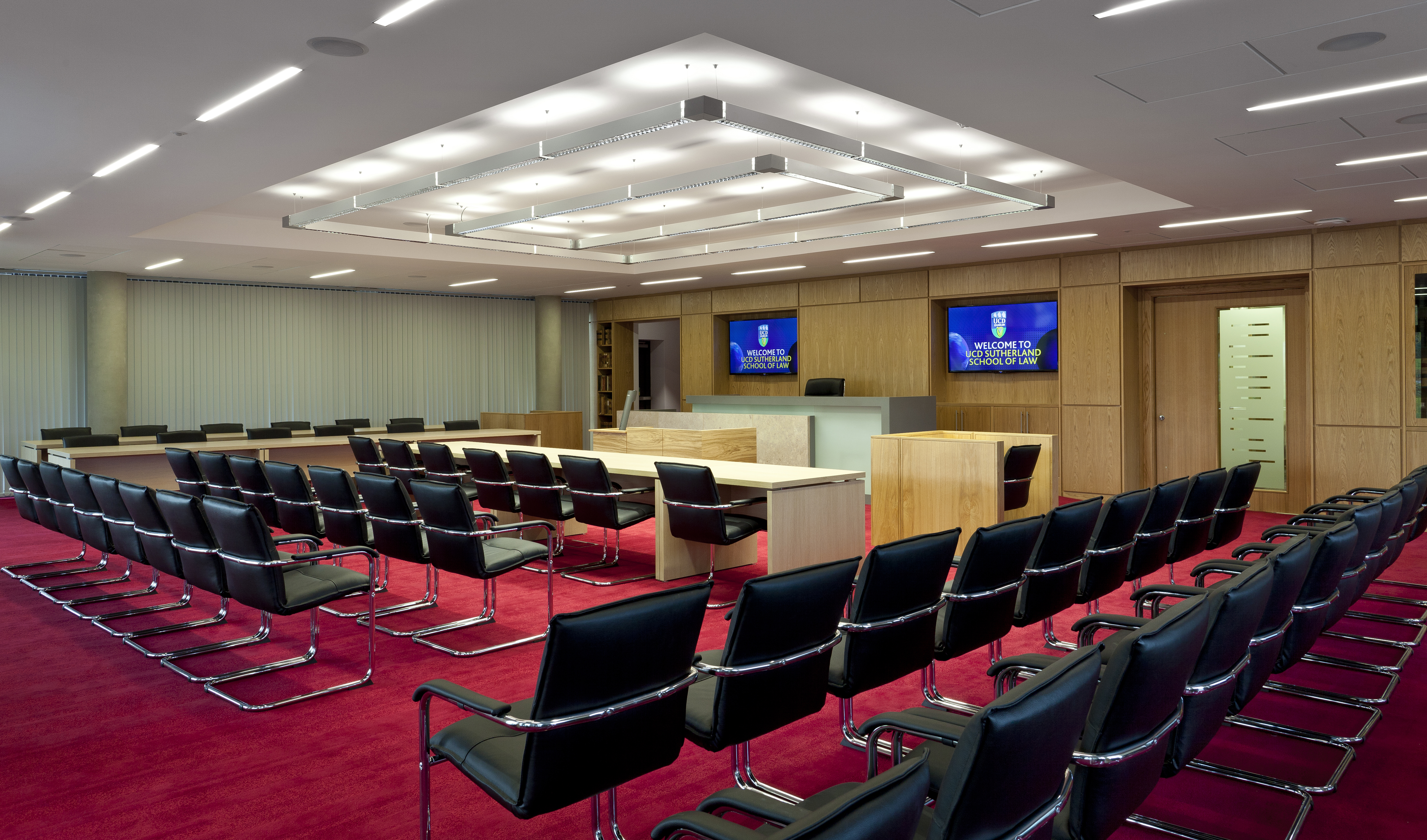 Rows of chairs facing the top of a room with screens behind a desk